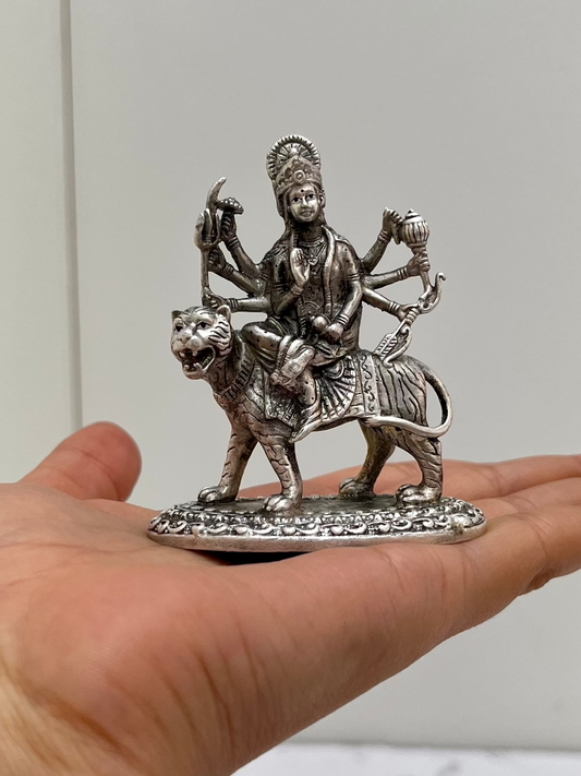 Silver statue of a deity on a lion held in a hand against a neutral background