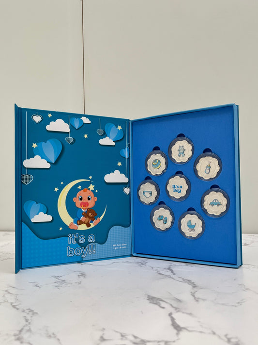 Set of baby shower decorations in a blue box with cartoon character and text 'it's a boy!' on a marble surface.