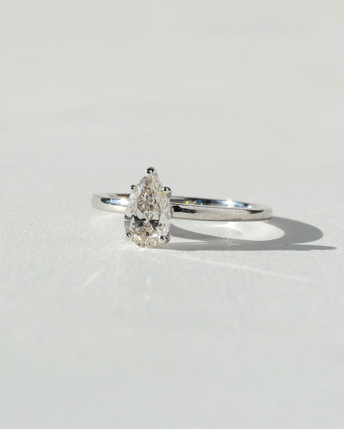 Diamond ring with pear-shaped gemstone on a light gray background