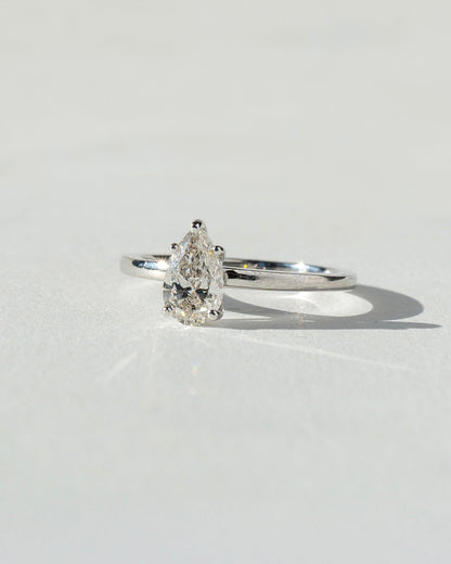 Diamond ring with pear-shaped gemstone on a light gray background