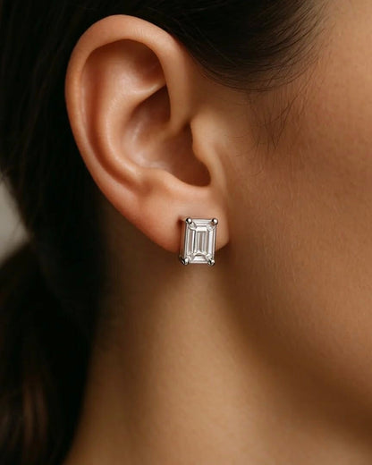 Close-up of emerald solitaire earring worn on ear – elegant gold emerald diamond studs