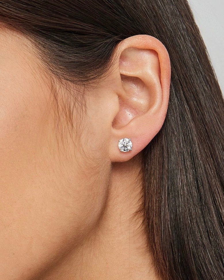 Close-up of round solitaire earring worn on ear – elegant gold round diamond studs